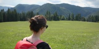 年轻女孩背着背包，穿过绿色的草地，背景是群山