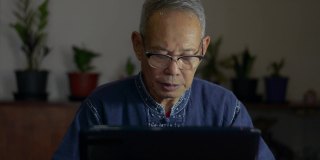 疲惫的亚洲老人坐在办公桌前，摘下眼镜，放下笔记本电脑，按摩太阳穴，缓解长期使用现代设备后的疲劳。由于电脑工作过度而头痛。