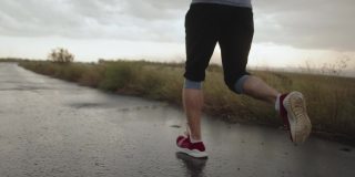 运动员穿着红色运动鞋在乡间沥青路上奔跑，雨后景色。一名男子在雨天跑马拉松