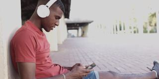 年轻的非洲裔美国人在户外戴着耳机使用手机的侧面