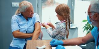 奶奶和孙女在医院里接种疫苗。一个小女孩扮演医生，给一个年长的妇女接种疫苗。小儿科医生用玩具注射器让孩子放松