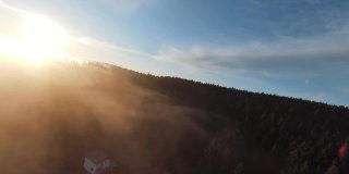 在晨雾中飞过薄雾的森林，在日出时，阳光照射在树梢。航拍在fpv无人机云朵自然景观与山地丘陵地形。电影的看法。