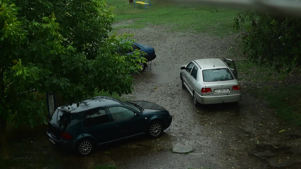 下雨了。女人下了车，走过水坑里的第二辆车。