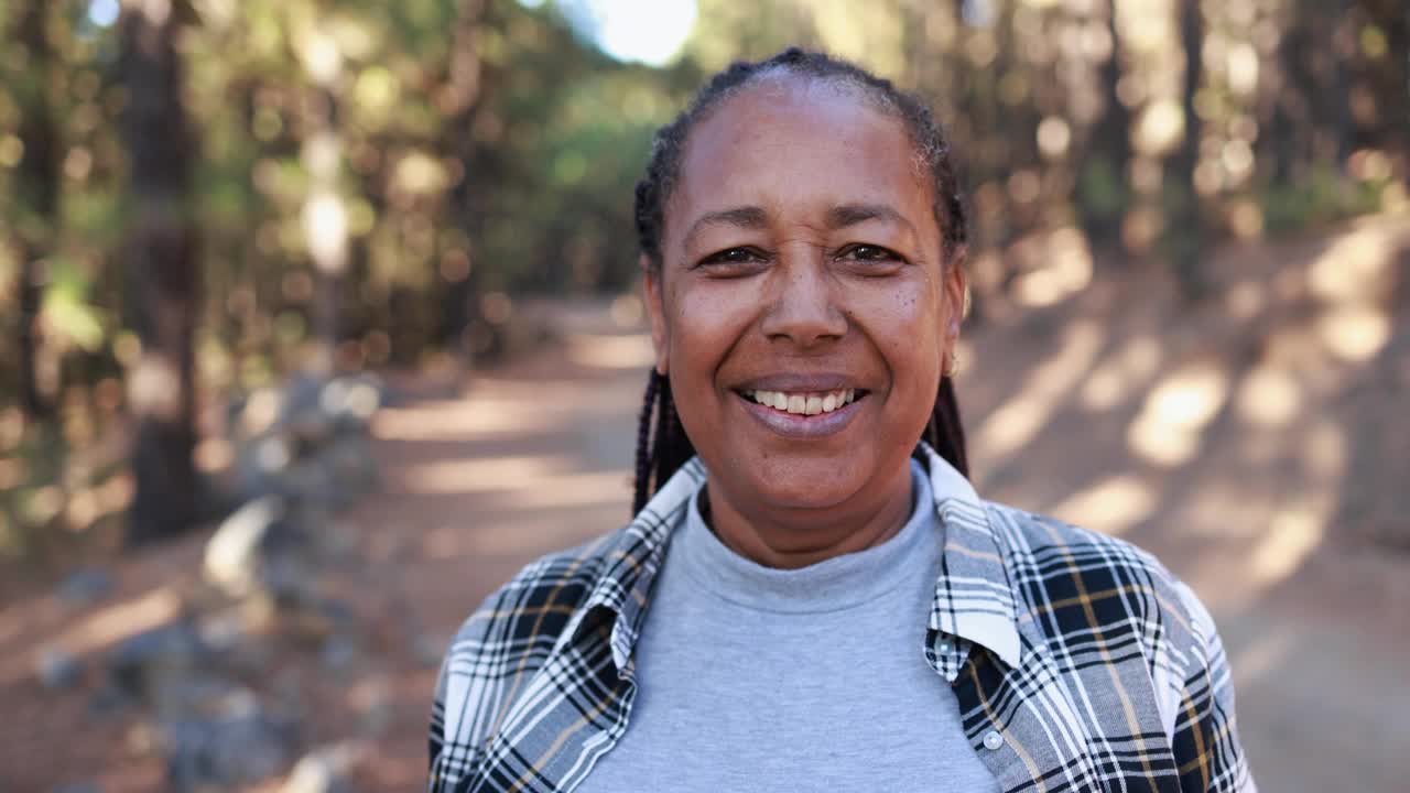 成熟的非洲裔美国妇女在镜头前微笑，背景是森林