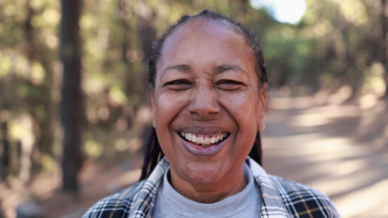 成熟的非洲裔美国妇女在镜头前微笑，背景是森林