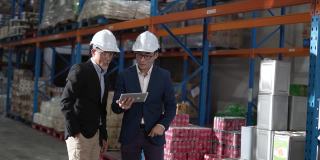 亚洲华人管理人员在仓库用数码平板电脑与白帽公司讨论