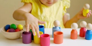 女孩通过玩一个小男人的彩色木制玩具来学习颜色，并把它们放在相应颜色的杯子里