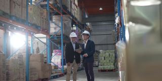 亚洲华人管理人员在仓库用数码平板电脑与白帽公司讨论