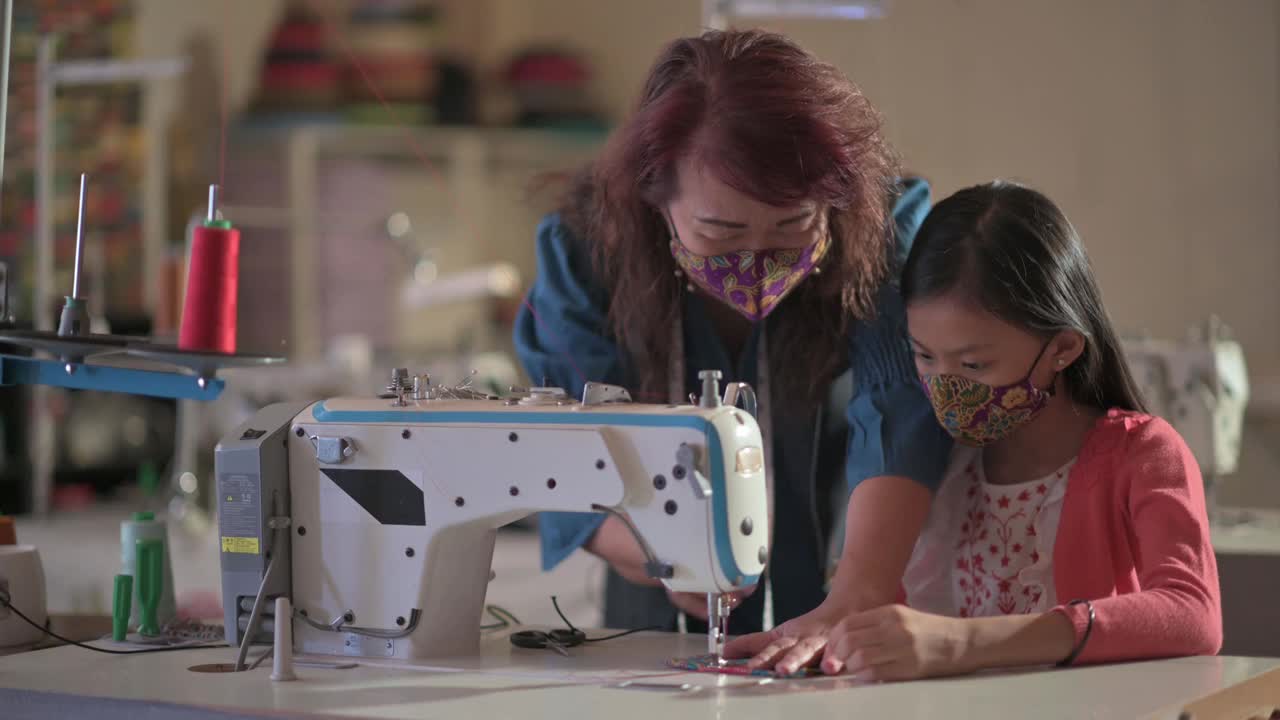 亚裔华裔女教师在工作室教育课上指导年轻女学生用缝纫机缝制蜡染布防护口罩