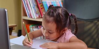 可爱的小女孩在家在线学习数学作业，在冠状病毒爆发期间保持社交距离。网络教育或家庭教育的概念。