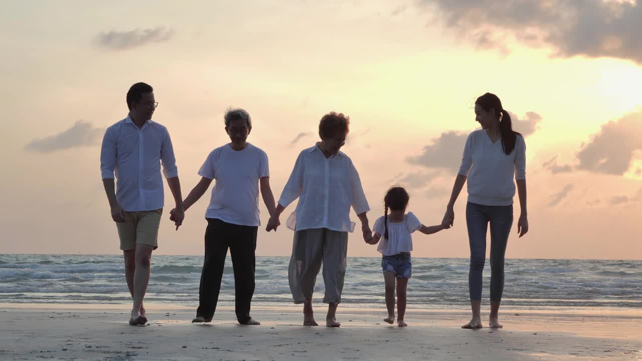 剪影中，快乐的亚洲大家庭五人手牵着手，走向日落海边的沙滩冲浪。幸福在自然的概念。