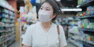 购物在新冠疫情蔓延，亚洲女性成年女性戴口罩防护手拉购物车在百货商店货架上购买消费品新常态生活方式