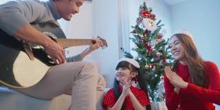亚洲可爱的家庭成员在家里一起享受唱圣诞歌曲。年幼的女儿心情愉快，兴奋地和父母一起在家里庆祝节日圣诞节感恩节聚会。