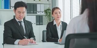 亚洲集团招聘人员在办公室面试应聘者。有吸引力的漂亮男人和女人人力资源经理坐在桌子上，在工作场所用笔记本电脑看简历和女孩谈工作申请。