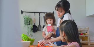 亚洲忙碌的母亲打电话，和女儿在厨房做饭。幸福的家庭，爱美丽的父母，妈妈和小妹妹感到幸福，享受在家里的时间。健康食品的概念