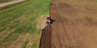 红色拖拉机正用耙子松动地面，保护土壤，平整表面，消灭杂草，准备季节性种植小麦，无人机从高空拍摄，从后面看