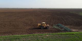 拖拉机用耙子在地里干活，转身离开了。松动地面，保护土壤，平整其表面，准备种植小麦和消灭杂草，无人机射击