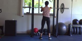 强壮的民族妇女在家庭健身房用杠铃锻炼