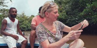斯里兰卡本托塔河上的一名游客，在两名当地导游的陪同下，她在船上用智能手机拍照。