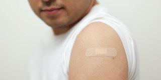 预防接种运动。年轻的印度男子接种了冠状病毒疫苗，在隔离的白色背景上展示了用绷带贴着的手臂。他给出了ok的信号