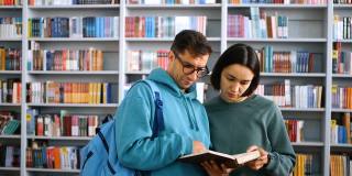 一名戴着眼镜的千禧一代年轻学生和一名年轻貌美的女学生站在图书馆书架的背景下看书备考。概念