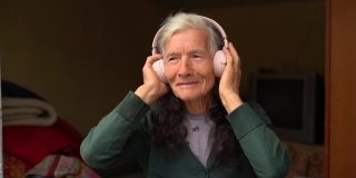 老年人和科技。村里的退休老人，用无线耳机听音乐。退休快乐，人和小玩意。老妇人戴着无线耳机