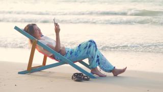 4K美丽的亚洲女人在日落时躺在海边的沙滩椅上视频素材模板下载