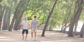 夏日清晨，4K亚洲老人和成年儿子一起在海滩上做运动。