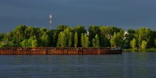 驳船，一艘货船沿河航行，沿岸绿树成荫。水路运输的概念