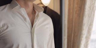 穿着夹克的时髦男子系好扣子，扣上白衬衫，准备靠窗出去