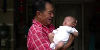 一个亚洲爷爷抱着他刚出生的孙子回家