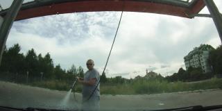 一个男人正在用高压水枪清洗汽车。水在挡风玻璃上缓慢飞溅