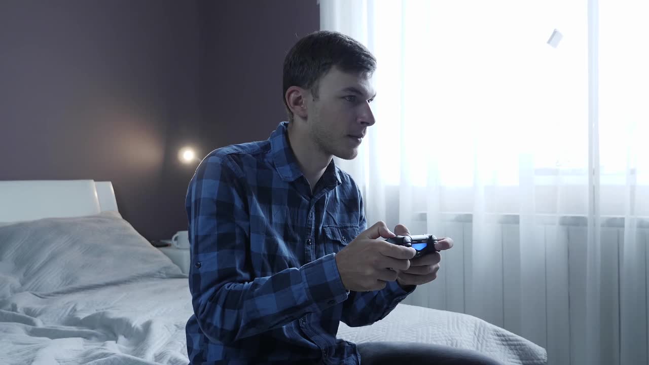 男人用手柄玩电子游戏。年轻的男性玩家在家里用无线操纵杆玩电子游戏。数字技术