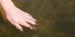 近景上女人的手轻轻地触摸着水面的河水。女人的手让手指穿过水。慢动作全高清视频