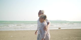 亚洲老夫妇手牵着手一起走在沙滩上，在夏天的日落。