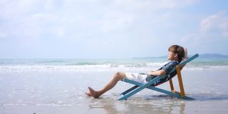 在夏日阳光明媚的日子里，一名亚洲男子躺在沙滩椅上休息。