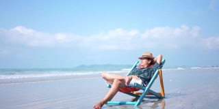 在夏日阳光明媚的日子里，一名亚洲男子躺在沙滩椅上休息。