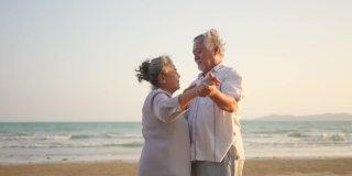4K亚洲老年夫妇在夏日日落的海滩上享受浪漫的假期，翩翩起舞