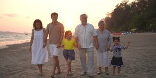 4K多代亚洲家庭手牵着手，在夏日日落的海滩上一起散步