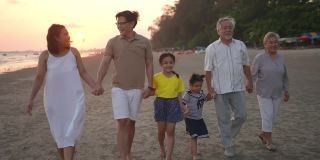 4K多代亚洲家庭手牵着手，在夏日日落的海滩上一起散步