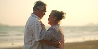 4K亚洲老年夫妇在夏日日落的海滩上享受浪漫的假期，翩翩起舞