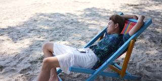 在夏日阳光灿烂的日子里，4K亚洲男人睡在沙滩椅上。