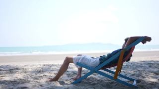 在夏日阳光灿烂的日子里，4K亚洲男人睡在沙滩椅上。视频素材模板下载