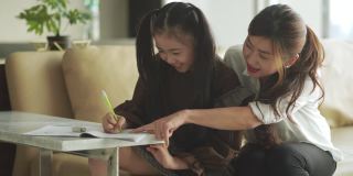 亚洲华人年轻的家庭母亲和女儿周末在客厅公寓里做家庭作业，享受亲子时光