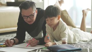 亚洲华人年轻的父亲和儿子周末在家里客厅公寓里画画，享受亲子时光视频素材模板下载