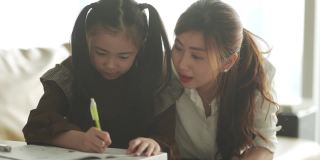 亚洲华人年轻的家庭母亲和女儿周末在客厅公寓里做家庭作业，享受亲子时光