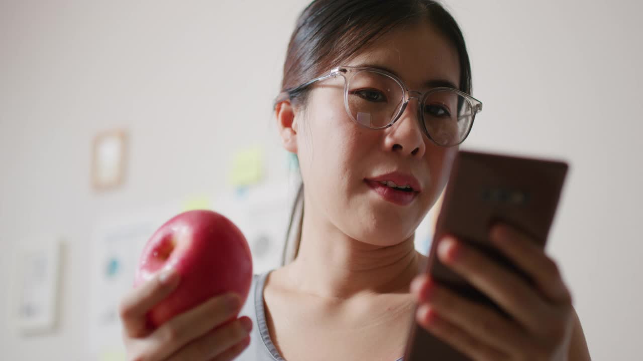年轻健康的女性一边吃苹果一边用手机