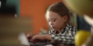 可爱的小女孩坐在舒适的客厅里，在笔记本电脑键盘上打字。