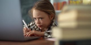 特写的严肃的小学女孩做家庭作业，在笔记本上写笔记，在笔记本上打字。