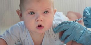 儿科医生为新生儿接种疫苗。疫苗，婴儿疫苗护士手中柔软的聚焦注射器和婴儿背景模糊的白色婴儿。戴着蓝色手套的医生，过来。